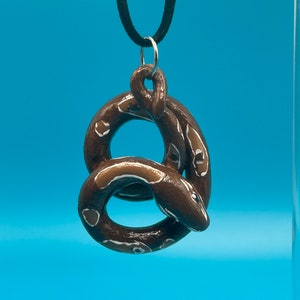 May include: A brown and white snake charm necklace with a black cord. The snake is curled into a circle shape.