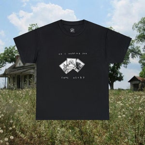 May include: Black t-shirt featuring a graphic of three Polaroid photos. The photos depict a woman with a creepy smile. The text on the shirt reads "am i making you feel sick?"