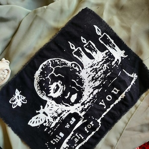 May include: Black fabric patch featuring a white graphic of a baby's head, candles, and a stylized insect. The text "this was all for you" is printed in white. The patch has a raw, unfinished edge.