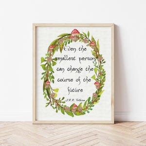 Op de afbeelding: Een ingelijste print met een citaat van J.R.R. Tolkien: "Zelfs de kleinste persoon kan de loop van de toekomst veranderen." Het citaat staat in een aquarelkrans van groene bladeren, rode paddenstoelen en kleine bloemen.