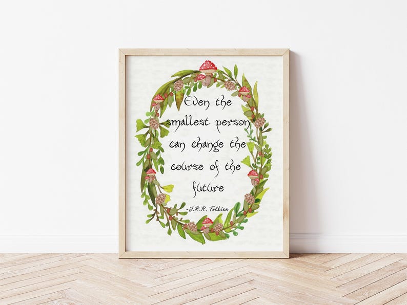 Op de afbeelding: Een ingelijste print met een citaat van J.R.R. Tolkien: "Zelfs de kleinste persoon kan de loop van de toekomst veranderen." Het citaat staat in een aquarelkrans van groene bladeren, rode paddenstoelen en kleine bloemen.