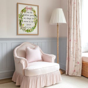 Op de afbeelding: Een lichtroze fauteuil met een gefranjerde rok en een bijpassend kussen. Een ingelijste print met een bloemenkrans en de quote "Even the smallest person can change the course of the future" hangt aan de muur. Een vloerlamp met een witte kap staat in de buurt.