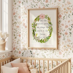 Op de afbeelding: Een ingelijste print met een bloemenkrans en de quote "Zelfs de kleinste persoon kan de loop van de toekomst veranderen" van J.R.R. Tolkien. De print zit in een licht houten frame, tegen een bloemenbehang.