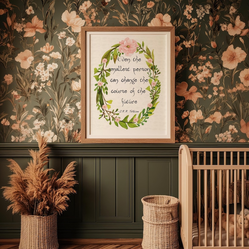 Op de afbeelding: Een ingelijste print met de quote "Zelfs de kleinste persoon kan de loop van de toekomst veranderen" omringd door een bloemenkrans. De print staat in een kamer met bloemenbehang en een wieg.