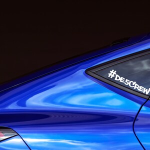 May include: A blue car with a white sticker on the back window that says "#DESCREW".