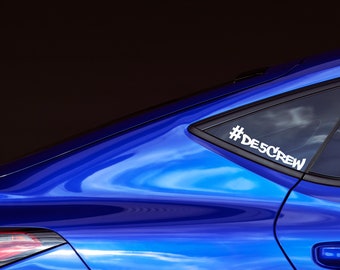 May include: A blue car with a white sticker on the back window that says "#DESCREW".