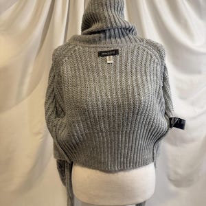 Puede incluir: Un su&eacute;ter gris recortado con cuello alto de canal&eacute;. El su&eacute;ter tiene mangas largas y una textura de punto acanalado. La etiqueta dice "URBAN OUTFITTERS". El su&eacute;ter se exhibe en un maniqu&iacute;.