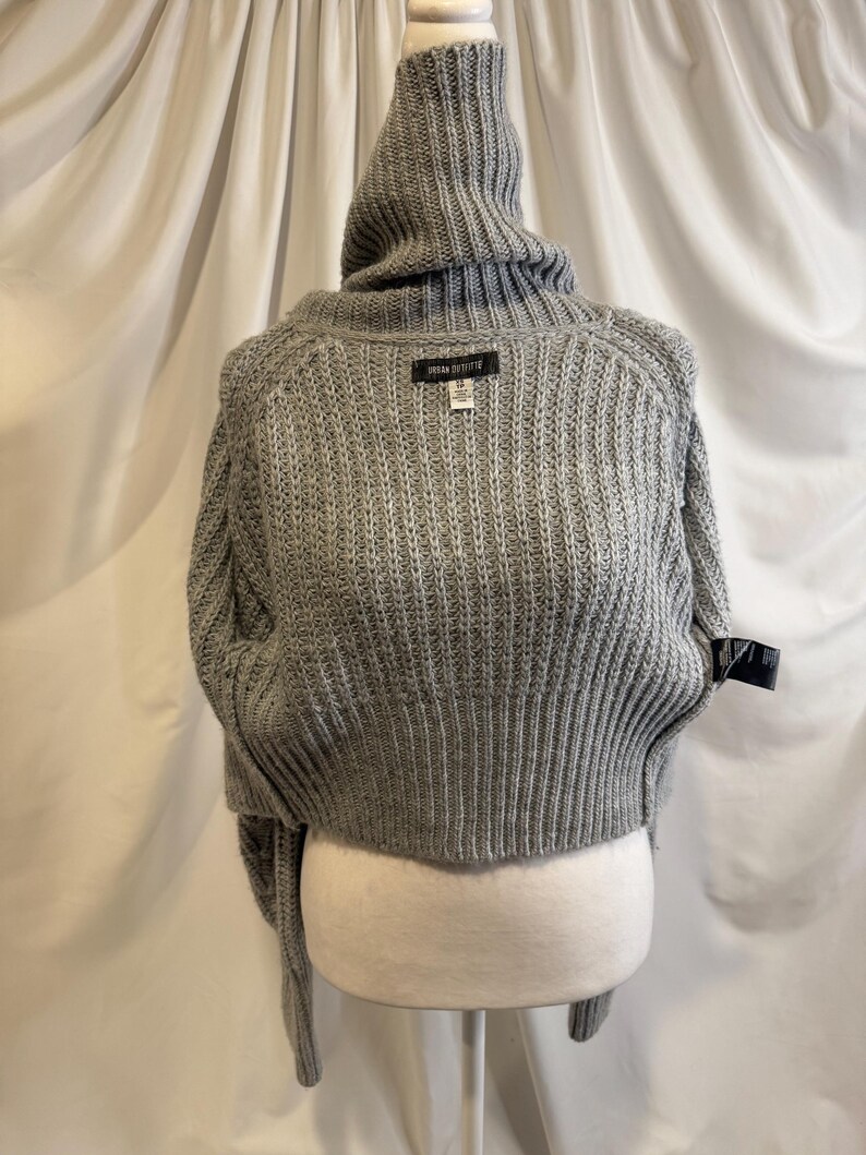 Puede incluir: Un su&eacute;ter gris recortado con cuello alto de canal&eacute;. El su&eacute;ter tiene mangas largas y una textura de punto acanalado. La etiqueta dice "URBAN OUTFITTERS". El su&eacute;ter se exhibe en un maniqu&iacute;.