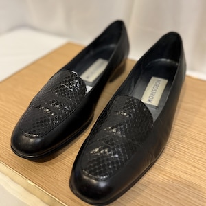 May include: A pair of black leather loafers with a snakeskin pattern on the vamp. The shoes have a square toe and a low heel. The brand name "Nordstrom" is visible on the insole. The shoes are displayed on a light brown wooden surface.
