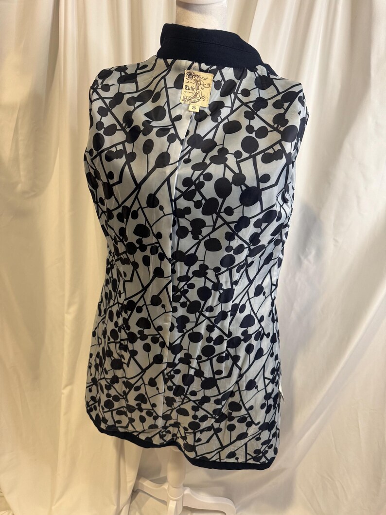 Puede incluir: Un chaleco azul marino con forro estampado en blanco y negro. El forro presenta un dise&ntilde;o de c&iacute;rculos y l&iacute;neas negras sobre un fondo claro. El chaleco se exhibe en un maniqu&iacute;.