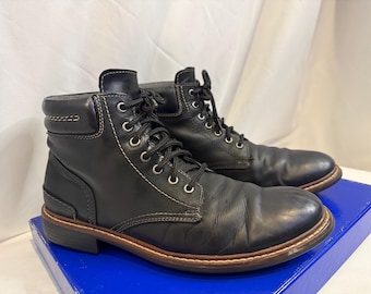 May include: A pair of black leather ankle boots featuring a rounded toe, a padded collar, and black laces threaded through silver-toned metal eyelets. The boots have visible tan contrast stitching along the seams and a dark brown sole edge.