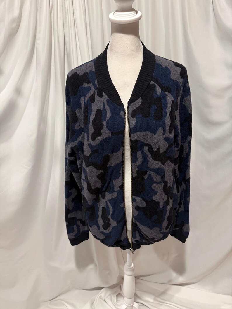 K&ouml;nnte beinhalten: Eine lang&auml;rmelige Bomberjacke mit Camouflage-Muster in Marineblau, Anthrazit und Schwarz. Die Jacke verf&uuml;gt &uuml;ber einen einfarbigen, schwarzen Rippstrickkragen, B&uuml;ndchen an den &Auml;rmeln und am Saum sowie einen durchgehenden Rei&szlig;verschluss in der Mitte.