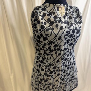 Puede incluir: Un blazer estampado en blanco y negro con cuello y ribete azul marino. El forro interior presenta un patr&oacute;n repetido de c&iacute;rculos y l&iacute;neas negras sobre un fondo gris claro. Una etiqueta es visible cerca del cuello.