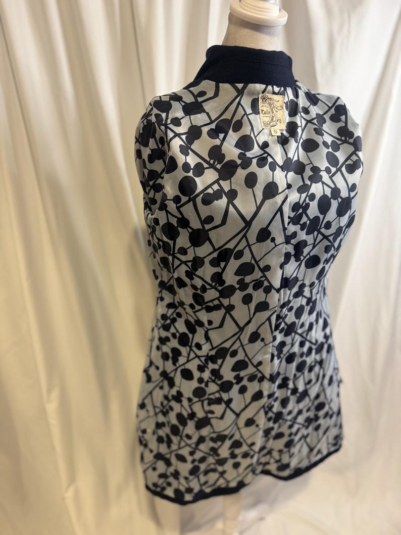 Puede incluir: Un blazer estampado en blanco y negro con cuello y ribete azul marino. El forro interior presenta un patr&oacute;n repetido de c&iacute;rculos y l&iacute;neas negras sobre un fondo gris claro. Una etiqueta es visible cerca del cuello.