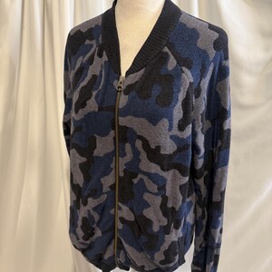 K&ouml;nnte beinhalten: Eine Bomberjacke mit Rei&szlig;verschluss und Camouflage-Muster in Marineblau, Hellblau und Schwarz. Die Jacke verf&uuml;gt &uuml;ber einen gerippten schwarzen Kragen, gerippte B&uuml;ndchen und einen durchgehenden Metallrei&szlig;verschluss in der vorderen Mitte.
