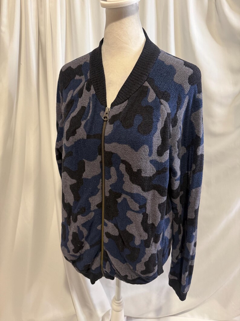 K&ouml;nnte beinhalten: Eine Bomberjacke mit Rei&szlig;verschluss und Camouflage-Muster in Marineblau, Hellblau und Schwarz. Die Jacke verf&uuml;gt &uuml;ber einen gerippten schwarzen Kragen, gerippte B&uuml;ndchen und einen durchgehenden Metallrei&szlig;verschluss in der vorderen Mitte.