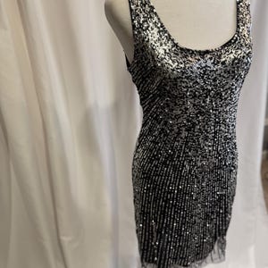 Pu&ograve; includere: Un abito senza maniche con paillettes e scollo rotondo. L'abito &egrave; nero e argento e ha una silhouette aderente.