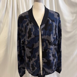 K&ouml;nnte beinhalten: Eine lang&auml;rmelige Bomberjacke mit Camouflage-Muster in Marineblau, Anthrazit und Schwarz. Die Jacke verf&uuml;gt &uuml;ber einen schwarzen Rippstrickkragen, B&uuml;ndchen und Saum sowie einen durchgehenden silberfarbenen Rei&szlig;verschluss auf der Vorderseite.