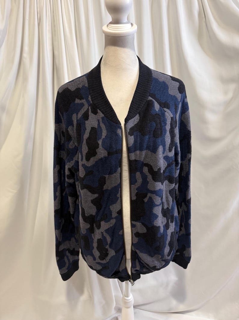 K&ouml;nnte beinhalten: Eine lang&auml;rmelige Bomberjacke mit Camouflage-Muster in Marineblau, Anthrazit und Schwarz. Die Jacke verf&uuml;gt &uuml;ber einen schwarzen Rippstrickkragen, B&uuml;ndchen und Saum sowie einen durchgehenden silberfarbenen Rei&szlig;verschluss auf der Vorderseite.