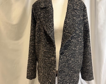 May include: A dark gray and beige textured coat with a notched collar and long sleeves. The coat is buttoned and displayed on a mannequin. The fabric has a speckled appearance.