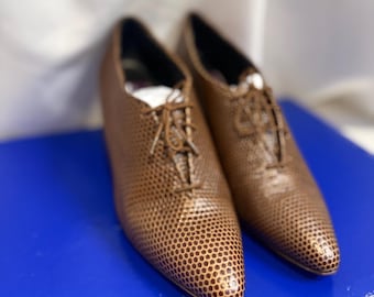 May include: A pair of bronze-colored lace-up shoes featuring a distinct, repeating circular dot pattern across the entire exterior surface. The shoes have a pointed toe design, thin matching laces, and a low-profile silhouette with a structured shape.