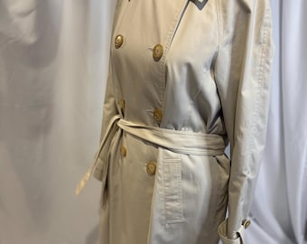 May include: A beige trench coat with a double-breasted design, featuring large buttons and a matching belt. The coat has a classic collar and adjustable cuffs. The coat is displayed on a mannequin.