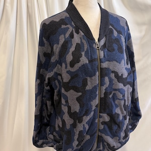 K&ouml;nnte beinhalten: Eine lang&auml;rmelige Bomberjacke mit Camouflage-Muster in Marineblau, Anthrazit und Schwarz. Die Jacke verf&uuml;gt &uuml;ber einen gerippten schwarzen Kragen, B&uuml;ndchen und Saum sowie einen durchgehenden Metallrei&szlig;verschluss an der Vorderseite.