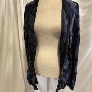 K&ouml;nnte beinhalten: Eine lang&auml;rmelige Jacke mit Rei&szlig;verschluss und Camouflage-Muster in Marineblau, Anthrazit und Schwarz. Das Kleidungsst&uuml;ck hat einen einfarbigen, schwarzen Rippkragen und passende Rippb&uuml;ndchen sowie einen durchgehenden Metallrei&szlig;verschluss.