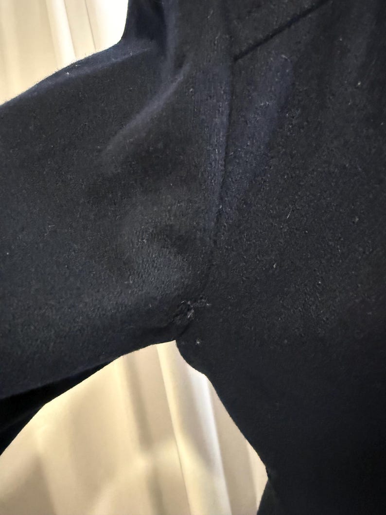 Puede incluir: Primer plano de una prenda azul marino oscuro, posiblemente un abrigo o una chaqueta, que muestra el hombro y la manga. La tela parece ser lana texturizada o un material similar. La costura del hombro es visible.