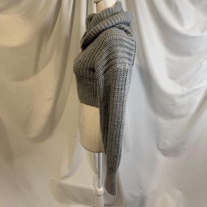 Puede incluir: Un su&eacute;ter corto gris con cuello alto se exhibe en un maniqu&iacute;. El su&eacute;ter est&aacute; hecho de un material grueso y tejido. Las mangas son largas y el dobladillo inferior del su&eacute;ter termina por encima de la cintura.
