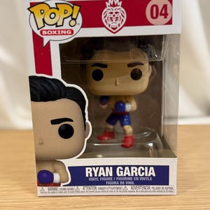 May include: A Funko Pop! vinyl figure of boxer Ryan Garcia in a clear plastic display case. The figure is wearing blue and red boxing attire. The box has the Funko Pop! Boxing logo and the number 04.