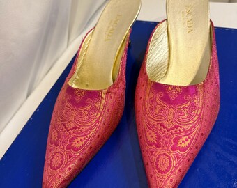 May include: A pair of Escada mules featuring a pointed toe and a vibrant fuchsia pink fabric upper with an intricate gold paisley pattern. The interior footbed is metallic gold and displays the brand name Escada and the text Made in Italy.