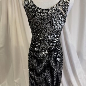 Pu&ograve; includere: Un abito senza maniche con paillettes, con un motivo nero e argento. L'abito ha un collo rotondo e una silhouette aderente.