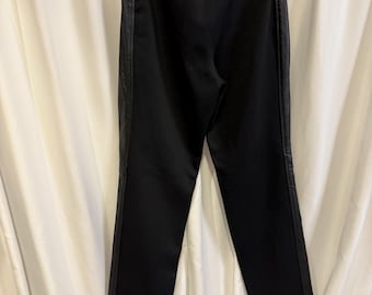 May include: Black pants with faux leather side panels. The pants are hanging on a hanger against a white curtain backdrop. The pants have a straight leg design and a high waist.