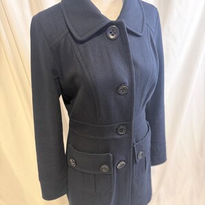 Puede incluir: Un abrigo azul marino con un dise&ntilde;o cl&aacute;sico. El abrigo presenta un cuello con solapas, cierres de botones y dos bolsillos delanteros. El abrigo se exhibe en un maniqu&iacute;.