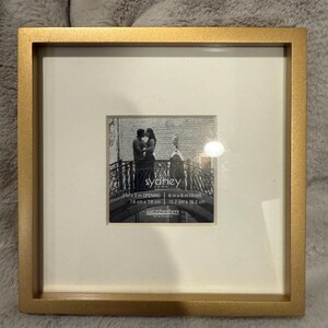 May include: Square gold-colored picture frame with a white mat. The frame holds a black and white photo of a couple. The opening is 3 inches by 3 inches, and the frame is 6 inches by 6 inches. The text "syaney" is visible.