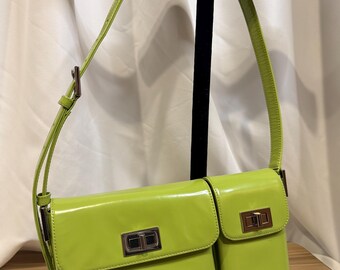 May include: A lime green shoulder bag with a rectangular shape and a smaller attached pocket. The bag has a shiny, patent leather-like finish and a silver-colored clasp. The strap is thin and adjustable.