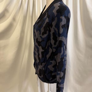 K&ouml;nnte beinhalten: Eine lang&auml;rmelige Strickjacke mit Camouflage-Muster in Marineblau, Anthrazit und Schwarz. Das Kleidungsst&uuml;ck verf&uuml;gt &uuml;ber einen einfarbigen, schwarzen Rippstrickbesatz an der Vorderseite, am Ausschnitt und an den &Auml;rmelb&uuml;ndchen sowie einen Rei&szlig;verschluss.