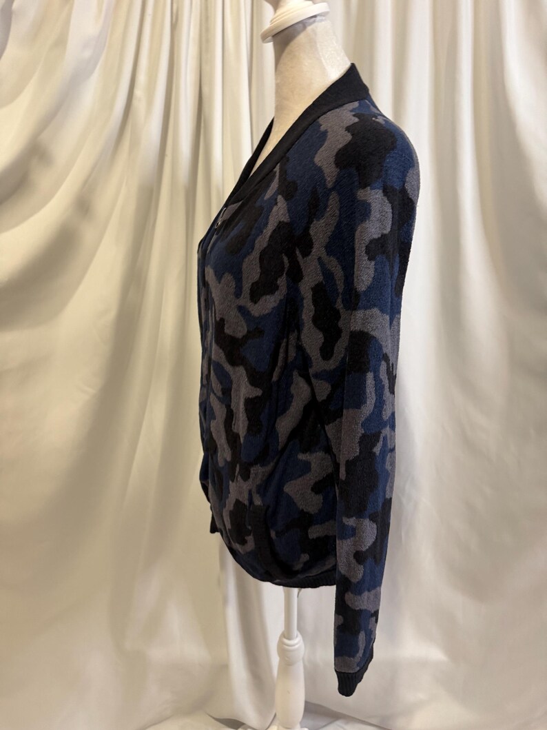 K&ouml;nnte beinhalten: Eine lang&auml;rmelige Strickjacke mit Camouflage-Muster in Marineblau, Anthrazit und Schwarz. Das Kleidungsst&uuml;ck verf&uuml;gt &uuml;ber einen einfarbigen, schwarzen Rippstrickbesatz an der Vorderseite, am Ausschnitt und an den &Auml;rmelb&uuml;ndchen sowie einen Rei&szlig;verschluss.