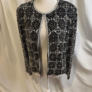 May include: A black open-front jacket featuring an intricate geometric pattern created with silver and white beads and sequins. The garment has long sleeves, a round neckline, and a repeating diamond motif covering the entire surface.
