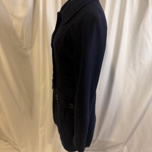 Puede incluir: Un abrigo azul marino oscuro con un dise&ntilde;o cl&aacute;sico. El abrigo presenta un cuello con muescas, cierres de botones y bolsillos. El abrigo se exhibe en un maniqu&iacute;, mostrando su ajuste a medida y su estilo. El abrigo es una pieza vers&aacute;til para el clima m&aacute;s fresco.