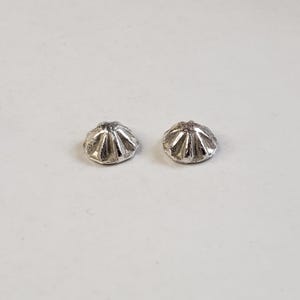 May include: Two small, silver-colored, flower-shaped beads. Each bead has a rounded, textured surface with multiple petal-like ridges radiating from the center. The beads are displayed on a plain, light-colored background.