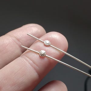 May include: Two silver-toned metal pins, each featuring a small, circular, textured accent piece positioned along the length of the straight, thin shaft. The circular elements have a sunburst-like pattern with radiating lines etched into the surface.