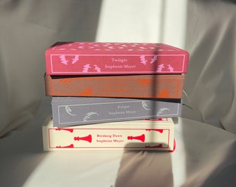 Puede incluir: Una pila de cuatro libros de bolsillo, todos del mismo autor, Stephanie Meyer. Los libros son Twilight, Luna Nueva, Eclipse y Amanecer. Los libros son todos de diferentes colores, con el libro superior de color rosa, el segundo libro de color marrón, el tercer libro de color gris y el libro inferior de color blanco.