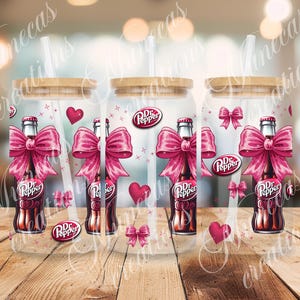 Puede incluir: Tres vasos de vidrio transparentes con tapa de bambú y pajita. Cada vaso presenta un lazo rosa con una botella de Dr Pepper en su interior. El fondo es una imagen borrosa de una superficie de madera.