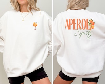 May include: White sweatshirt with an orange Aperol Spritz illustration on the front and the text "Aperol Spritz" on the back.