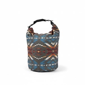 May include: A cylindrical dry bag featuring a dark gray base color with a repeating geometric pattern in shades of blue, orange, white, and brown. The bag includes a black plastic buckle closure at the top with an integrated metal D-ring attachment.