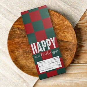May include: A rectangular coffee package with a green and red checkered pattern and the words "HAPPY holidays" in white. The package sits on a wooden plate, with a light-colored cloth and wooden table in the background. The package contains 12 oz of whole bean coffee.