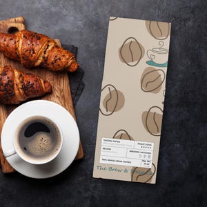 May include: Overhead shot of a coffee setup with a white cup of coffee on a saucer, two chocolate croissants on a wooden board, and a coffee bag. The bag is beige with coffee bean illustrations and the text "The Brew & Steep Co."