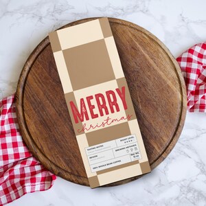 May include: A coffee bag with "MERRY christmas" in red script. The bag has a tan and brown checkered pattern and is on a wooden serving board. A red and white checkered cloth is on the side. The bag contains 12 oz of whole bean coffee.